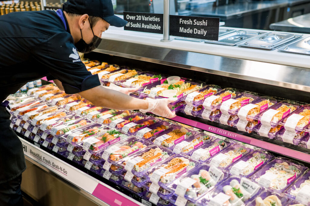 A man placing sushi boxes for display in a grocery store